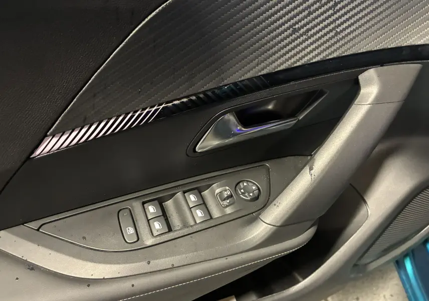 Gros plan sur la porte côté conducteur du Peugeot 2008 bleu 2025, montrant les commandes des vitres et la poignée intérieure.