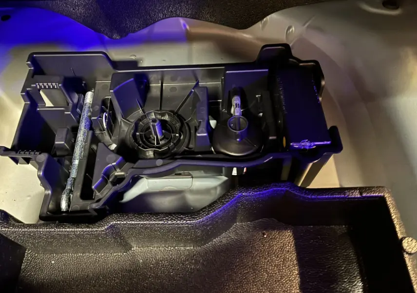 Vue rapprochée du rangement d'outils sous le plancher du coffre d'un Peugeot 2008 bleu 2025, avec support plastique noir.