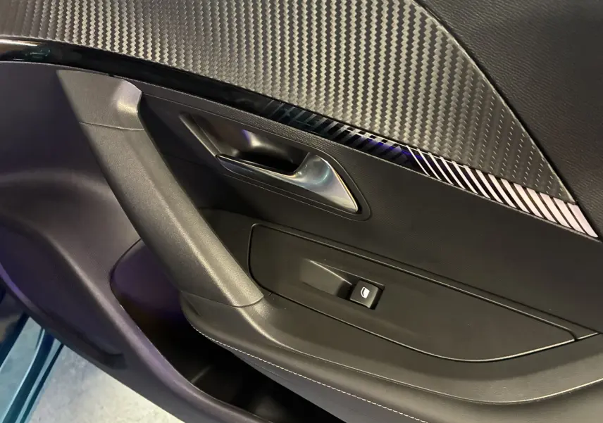 Détail de la porte intérieure côté gauche de la Peugeot 2008 1.2 Hybrid 136 Allure avec insert décoratif noir à effet carbone.