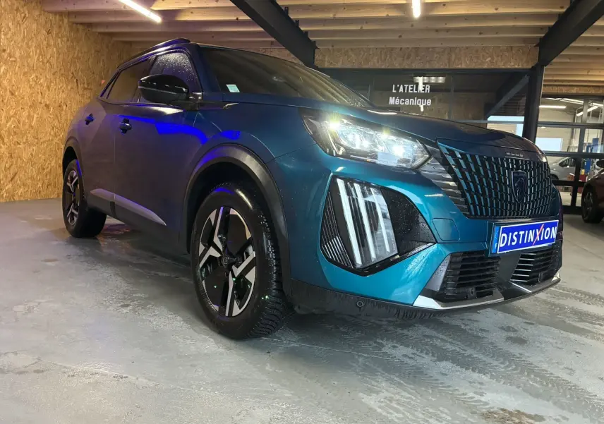 Vue 3/4 avant droit d'un Peugeot 2008 bleu hybride 2025 avec phares LED et calandre distinctive, stationné en intérieur.