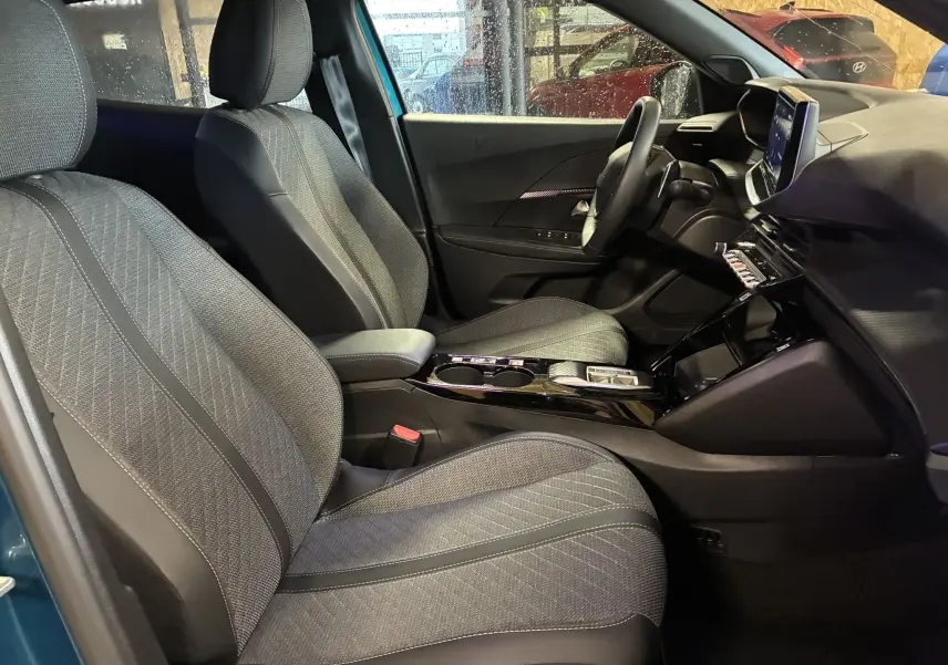 Vue intérieure côté conducteur du Peugeot 2008 bleu 2025, mettant en valeur les sièges tissu gris et la console centrale moderne.