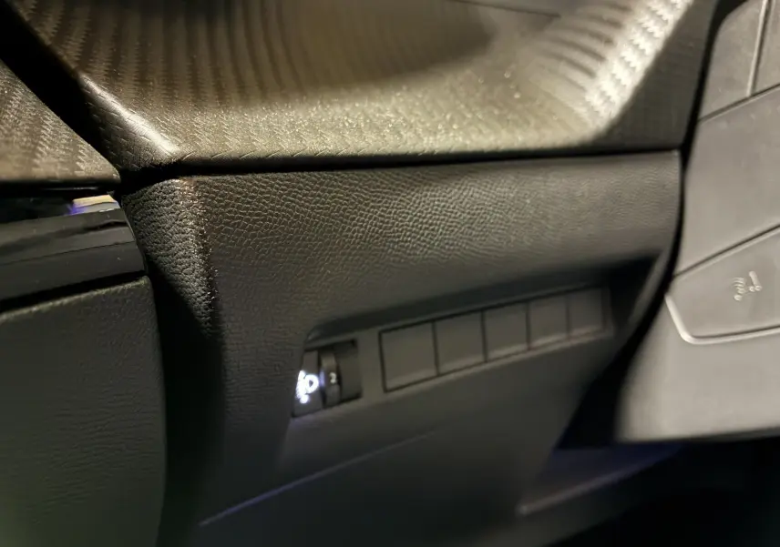 Gros plan sur la partie inférieure gauche du tableau de bord noir texturé du Peugeot 2008 1.2 Hybrid 136 Allure.