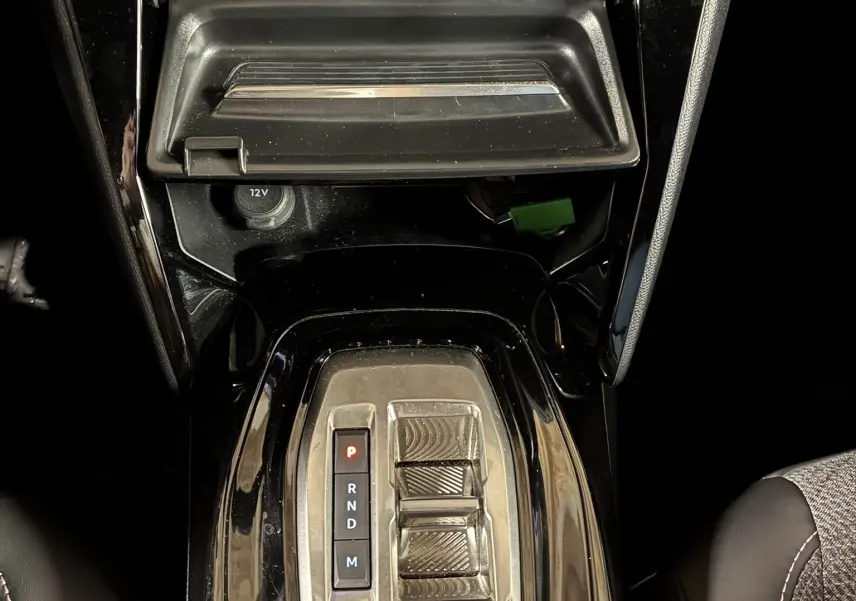 Vue plongeante sur la console centrale noire du Peugeot 2008 Hybrid 2025 avec levier de vitesses automatique et rangement ouvert.