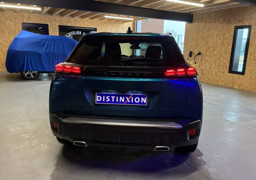Vue arrière d’un Peugeot 2008 bleu 2025 hybride avec feux LED allumés dans un garage éclairé.