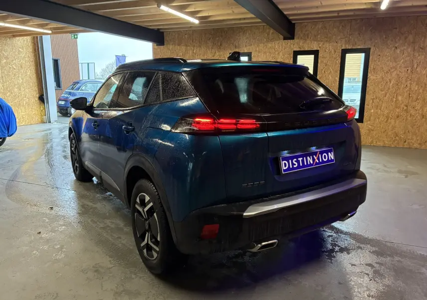Vue 3/4 arrière droite du Peugeot 2008 bleu hybride 2025 avec feux arrière allumés dans un garage.