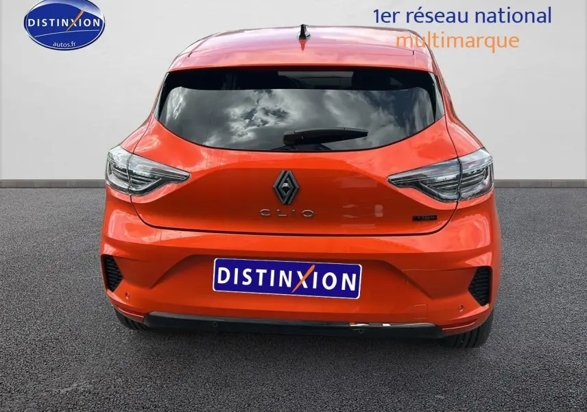 Vue arrière d'une Renault Clio V orange Valencia avec feux LED et logo central sur fond urbain gris.