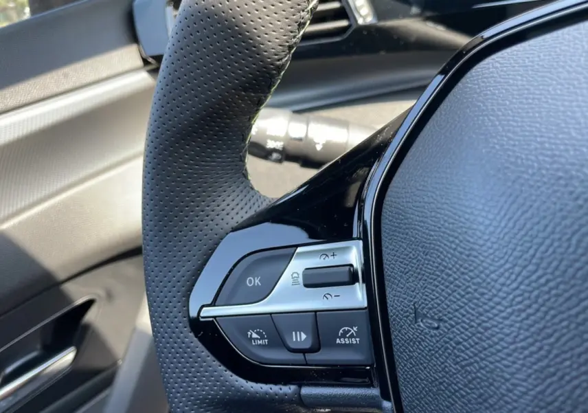 Gros plan sur le volant perforé noir de la Peugeot 308 1.5 HDI 130 EAT8 GT 2025, avec commandes intégrées et finition brillante.