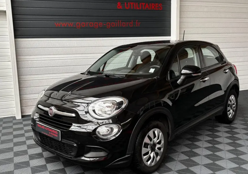 Vue 3/4 avant droit d'une Fiat 500X noire 2018 dans un garage avec sol carrelé gris et blanc.