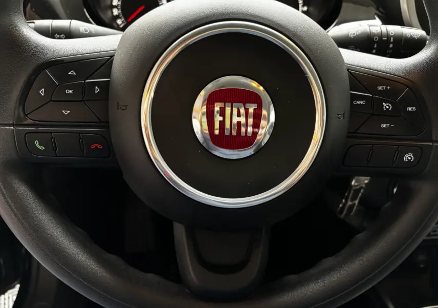 Gros plan sur le volant noir multifonctions avec logo FIAT rouge au centre du Fiat 500X 2018.