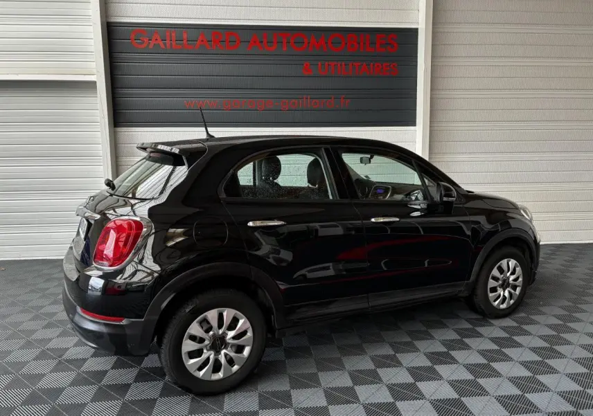 Vue de profil côté gauche d'une FIAT 500X noire 2018 garée en intérieur avec jantes argentées et feux arrière rouges.
