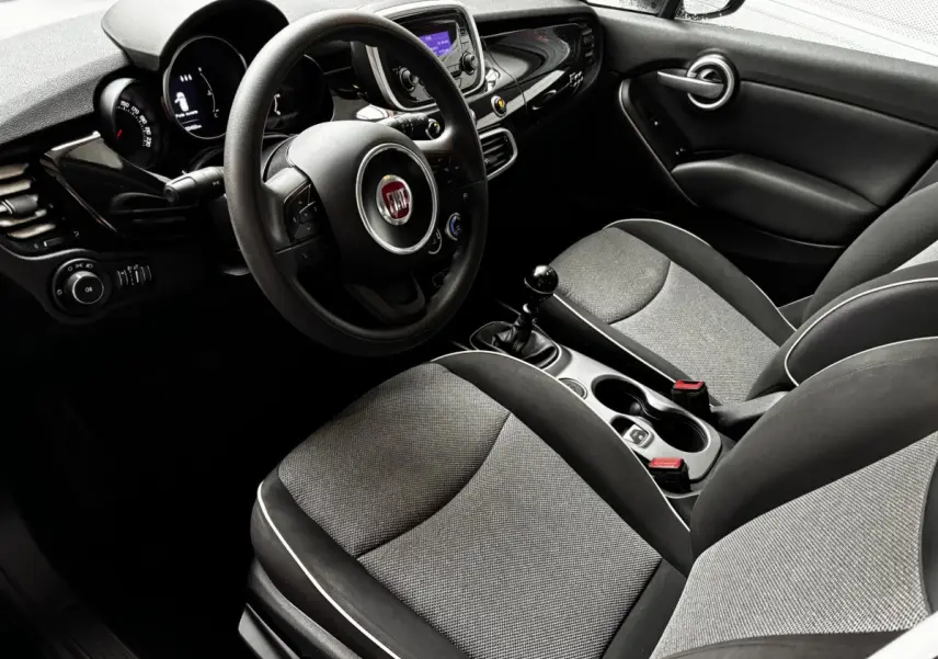Vue intérieure côté conducteur de la Fiat 500X noire, montrant le volant multifonctions et la console centrale avec boîte manuelle.