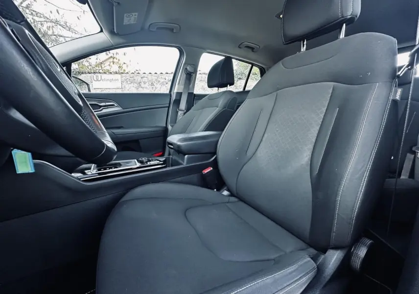 Vue intérieure côté conducteur du Kia Sportage 2023 noir, siège tissu avec accoudoir central et volant partiel visible.