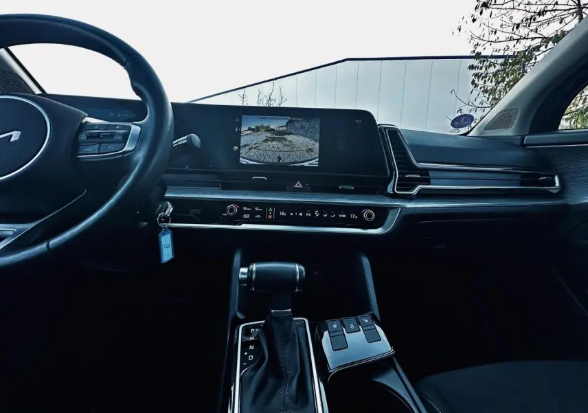 Vue intérieure du tableau de bord noir du Kia Sportage 2023 avec écran tactile affichant la caméra de recul et levier de boîte automatique.