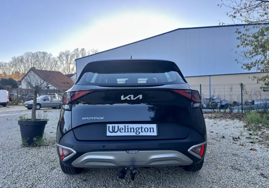 Vue arrière d'un Kia Sportage noir 2023 avec attelage et feux arrière LED distinctifs sur un sol gravillonné.