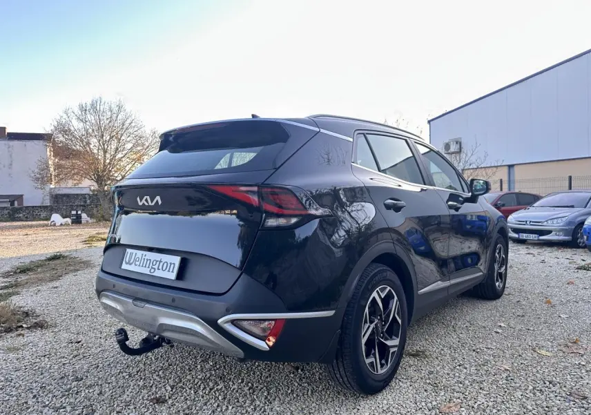 Vue 3/4 arrière droite du Kia Sportage noir 2023 avec feux arrière LED et attelage de remorque visible.