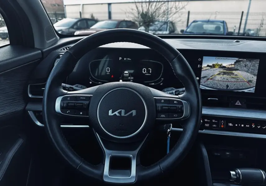 Vue intérieure centrée sur le volant KIA et l'écran tactile affichant la caméra de recul du Kia Sportage noir 2023.