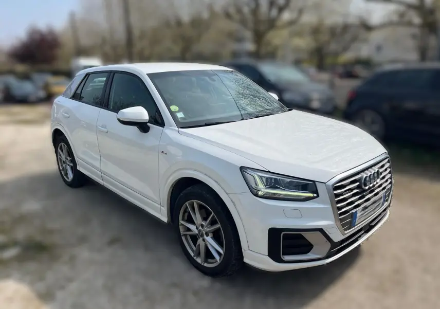 Audi Q2 blanc vue 3/4 avant droit, avec jantes alliage et calandre distinctive S-Line.
