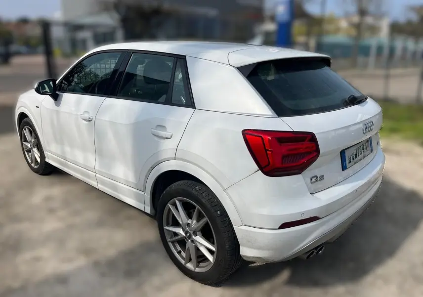 Audi Q2 blanc vue 3/4 arrière droit, avec jantes alu et feux arrière rouges distinctifs.