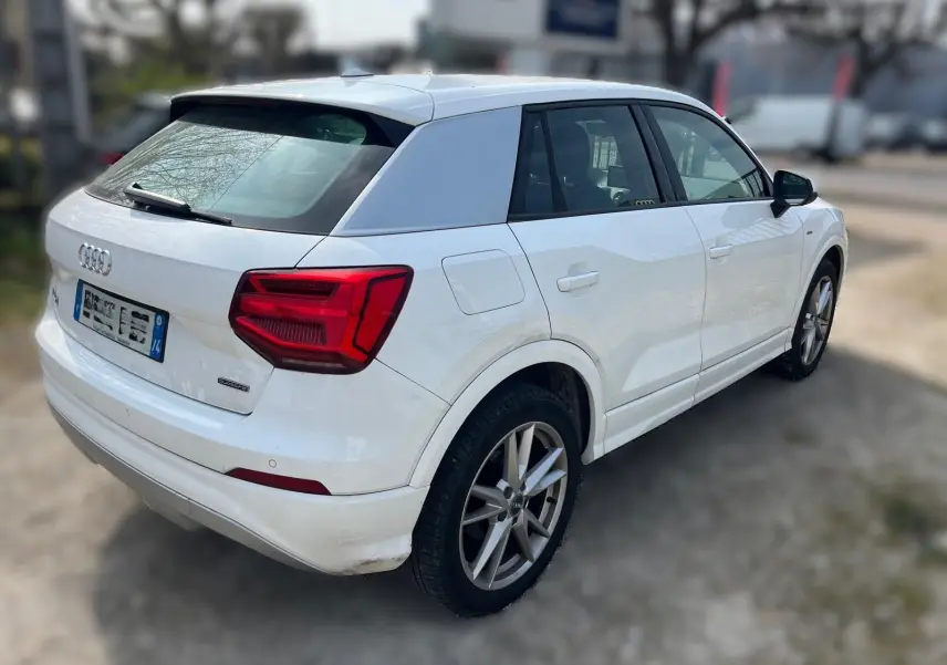 Audi Q2 blanc vue 3/4 arrière droit, avec jantes alu et feux arrière rouges bien visibles.