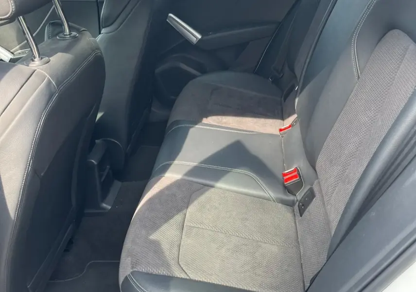 Vue intérieure côté arrière droit de l'Audi Q2 blanc, montrant la banquette en cuir et tissu noir avec ceintures rouges.