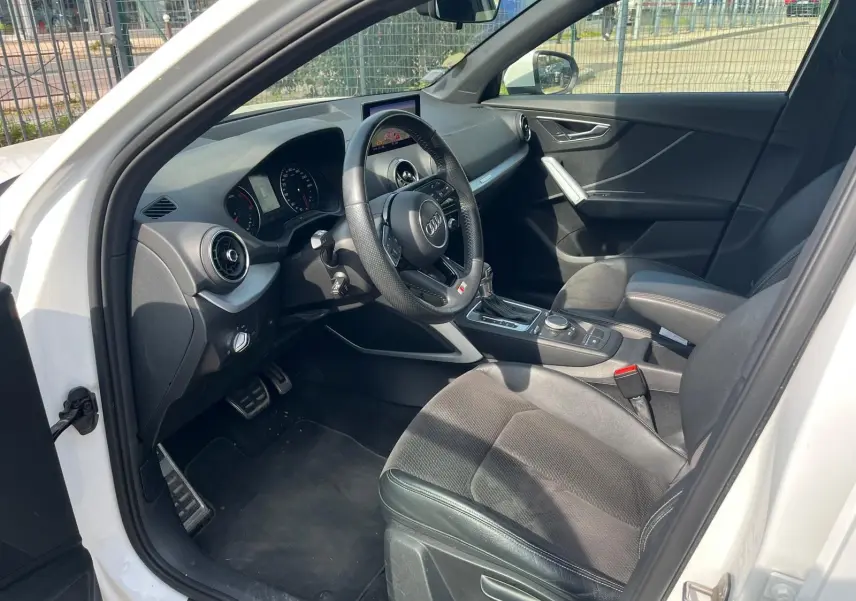 Vue intérieure côté conducteur de l'Audi Q2 blanche 2018, avec volant multifonction et sellerie noire en tissu et cuir.