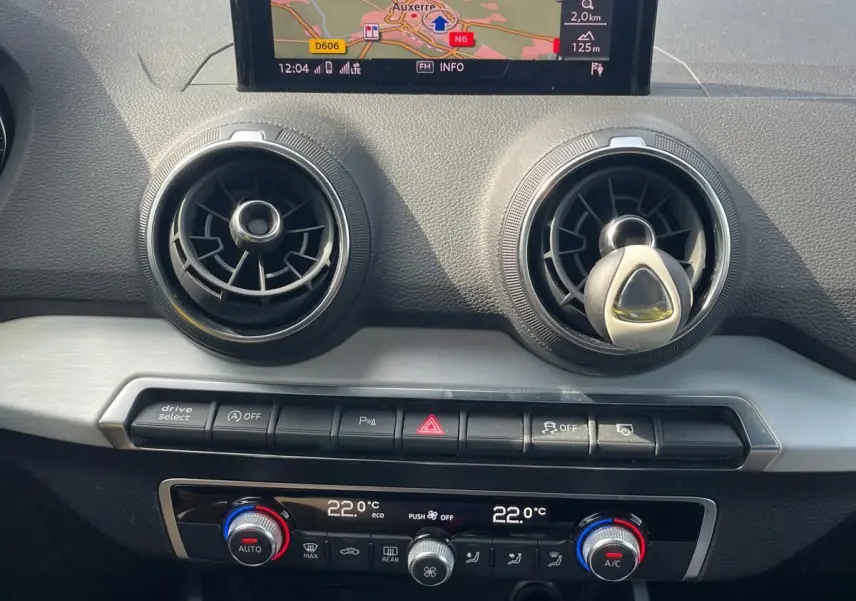 Vue rapprochée du tableau de bord de l'Audi Q2 blanc, avec écran GPS central et commandes de climatisation automatique.