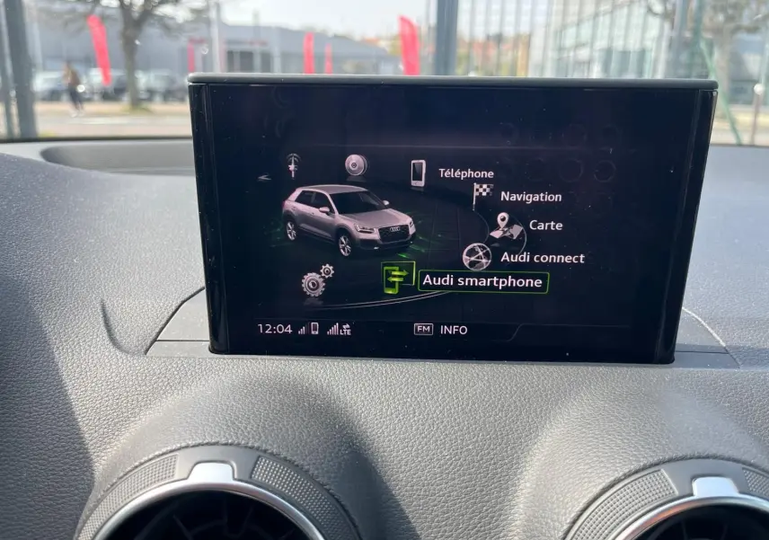 Écran central de l'Audi Q2 montrant le menu Audi smartphone avec vue intérieure sur tableau de bord noir.