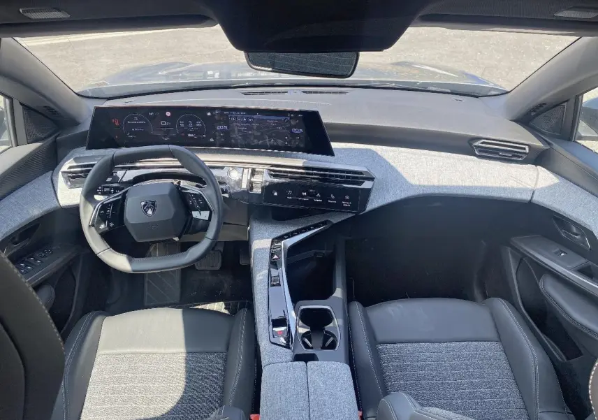 Vue intérieure avant du Peugeot 5008 Hybrid 145 allure e-dcs6 2025 avec tableau de bord numérique et sellerie tissu gris et cuir noir.