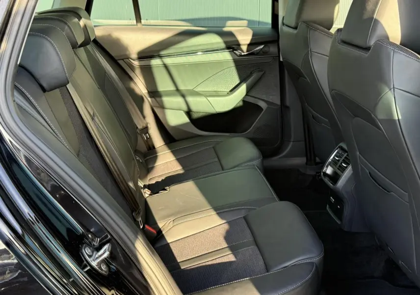 Vue côté gauche de l'intérieur arrière noir cuir et tissu de la Skoda Octavia Combi 2022 avec aérateurs et porte ouvert