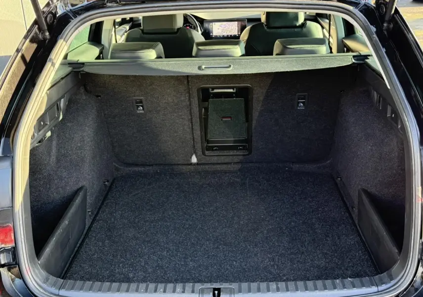 Coffre ouvert vu de l'arrière d'une Skoda Octavia Combi noire, avec tapis de sol gris et banquette arrière visible.
