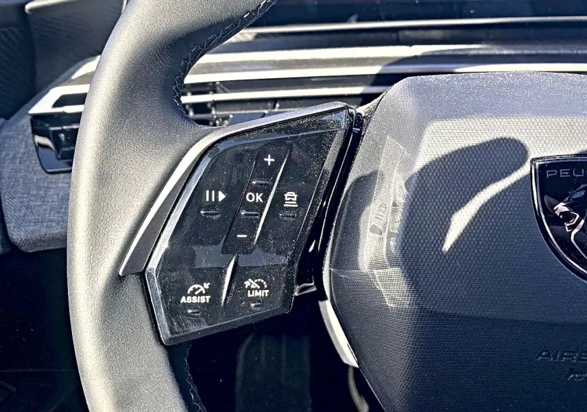 Gros plan sur le volant cuir noir de la Peugeot 5008 Hybrid 145 allure, avec commandes multifonctions à gauche.