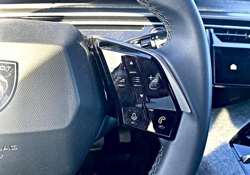 Gros plan sur le volant cuir noir du Peugeot 5008 Hybrid 145 avec commandes vocales et téléphone intégrées.