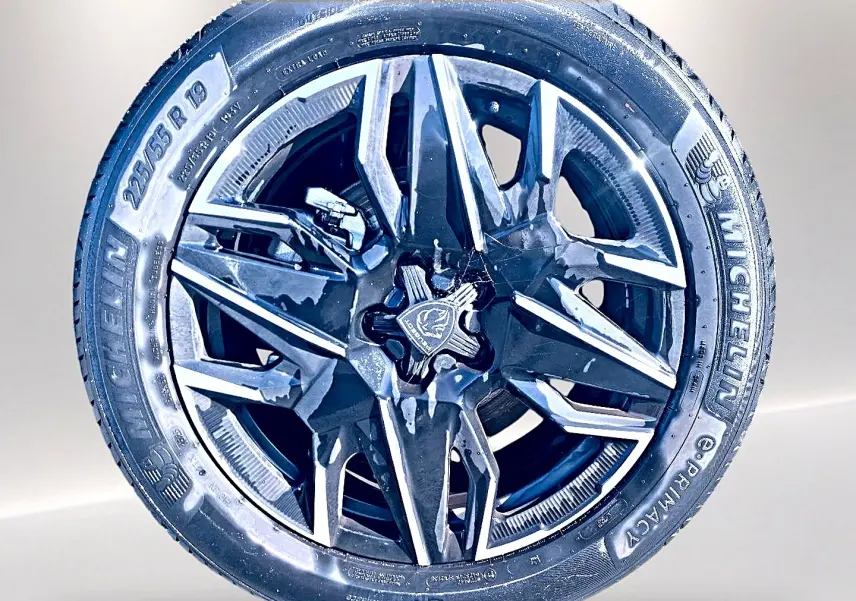 Gros plan sur la jante alu noire et argentée de la Peugeot 5008 Hybrid 145 allure e-dcs6 blanche, pneu Michelin 225/55 R19.