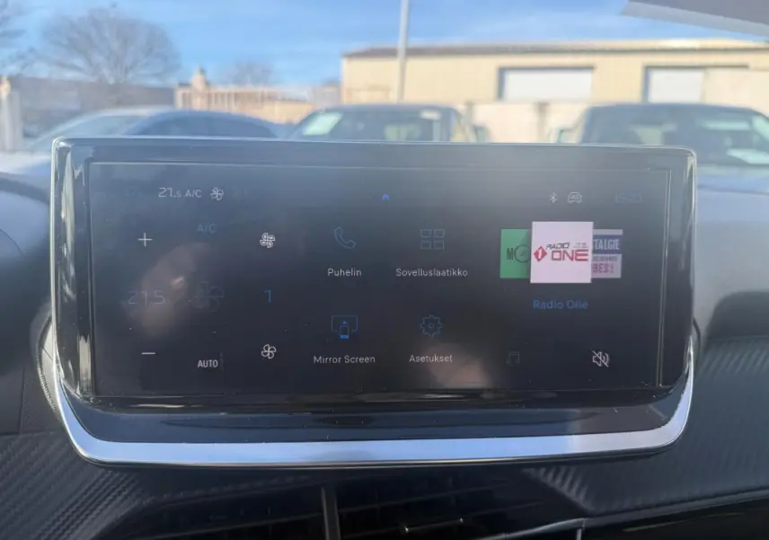 Écran tactile central de la Peugeot 208 Hybrid blanc, affichant les commandes climatisation et radio, vue intérieure frontale.