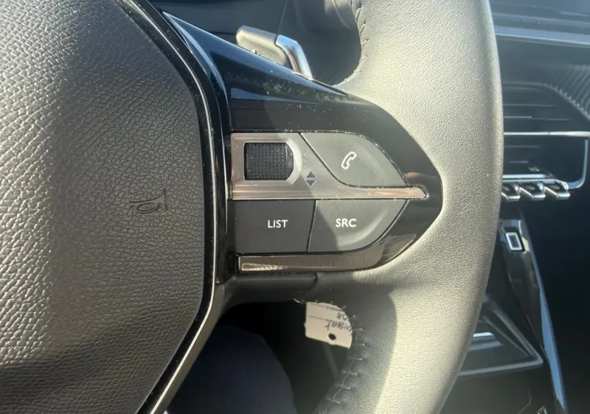 Gros plan sur les commandes gauche du volant noir de la Peugeot 208 Hybrid 110 e-DCS6 Allure 2024, avec boutons LIST et SRC.