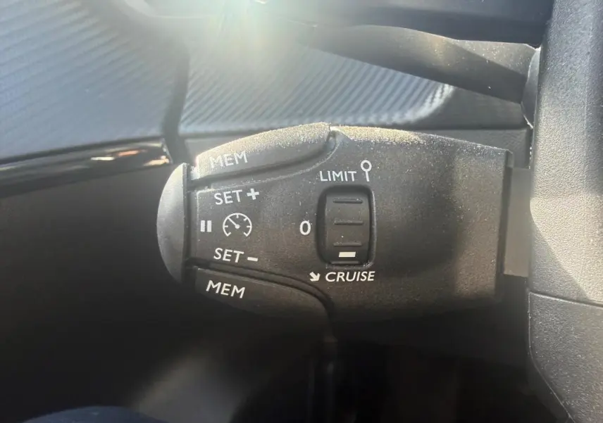 Gros plan sur la commande de régulateur de vitesse du Peugeot 208 Hybrid blanc, côté gauche du volant.