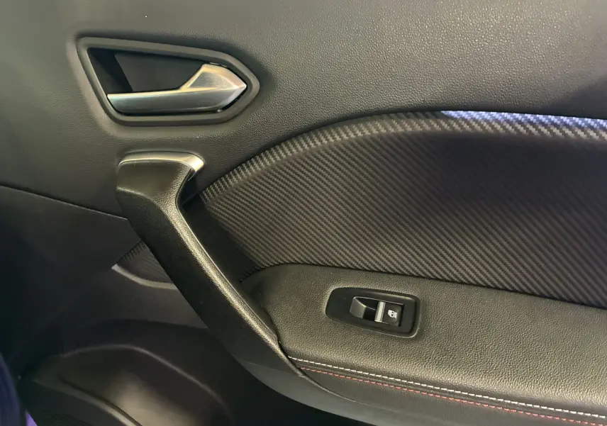 Détail de la porte intérieure côté gauche du Renault Captur 1.3 TCE 140 EDC RS Line 2021 avec insert carbone et bouton de vitre électrique.