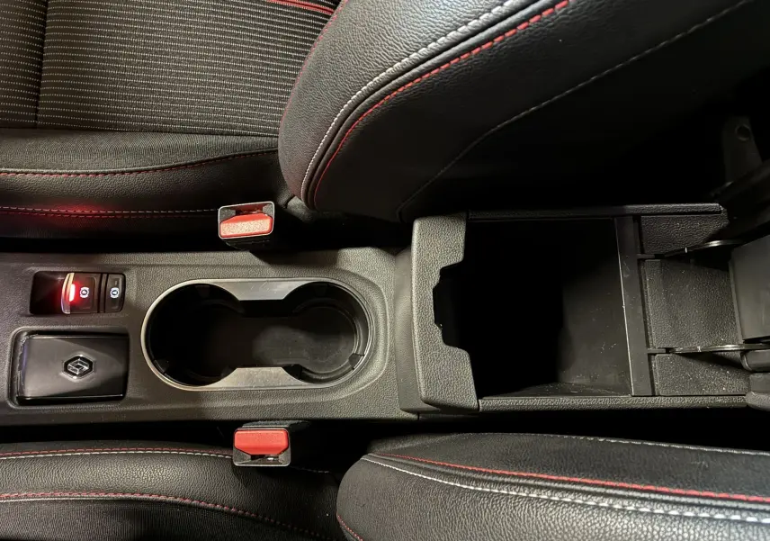 Vue rapprochée de la console centrale noire avec surpiqûres rouges du Renault Captur gris, montrant porte-gobelets et accoudoir ouvert.