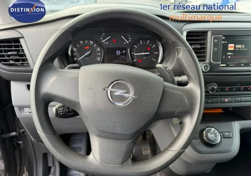 Vue intérieure centrée sur le volant Opel du Vivaro Fourgon gris Pierre de Lune, tableau de bord et écran multimédia visibles.