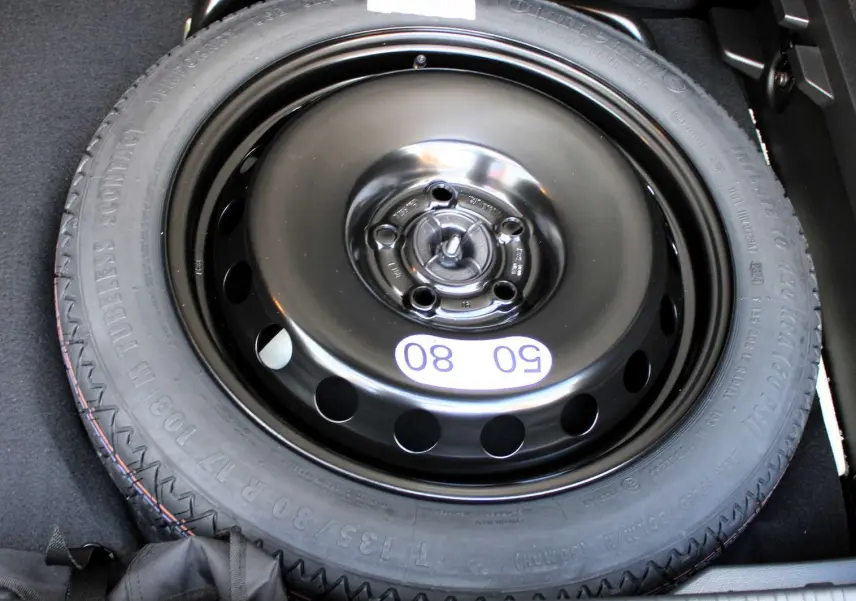 Roue de secours noire en gros plan dans le coffre d'un Renault Captur 2025 hybride noir métal avec toit gris.