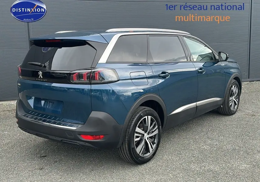 Vue 3/4 arrière droite d'un Peugeot 5008 bleu 2024 avec jantes alliage 18 pouces et vitres surteintées.