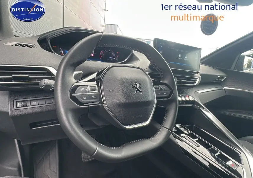 Vue intérieure du poste de conduite du Peugeot 5008 bleu, volant compact et écran tactile central visible.