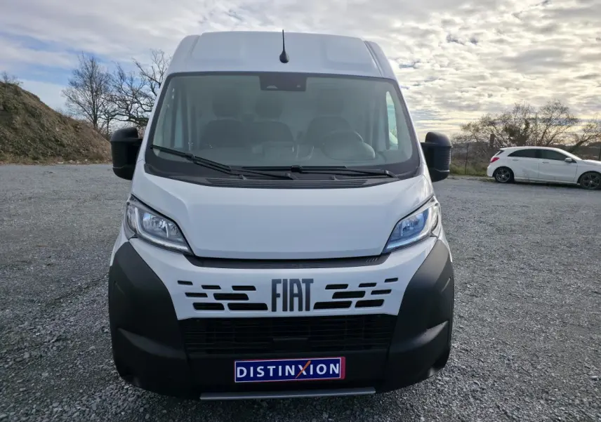 Vue de face du fourgon FIAT Ducato blanc avec pare-chocs noir et logo FIAT bien visible sur un parking extérieur.