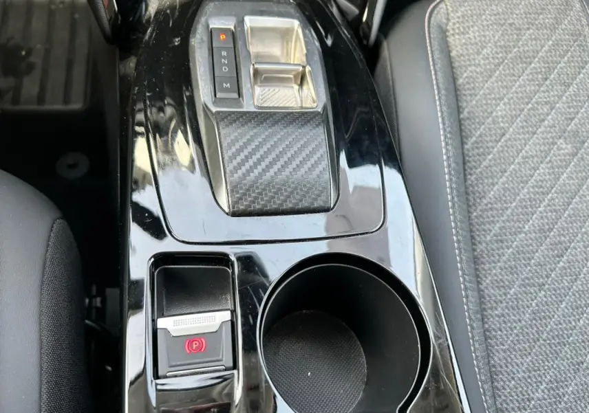 Vue rapprochée de la console centrale noire brillante avec sélecteur de boîte auto et frein à main électrique dans une Peugeot 208 gris 2024.