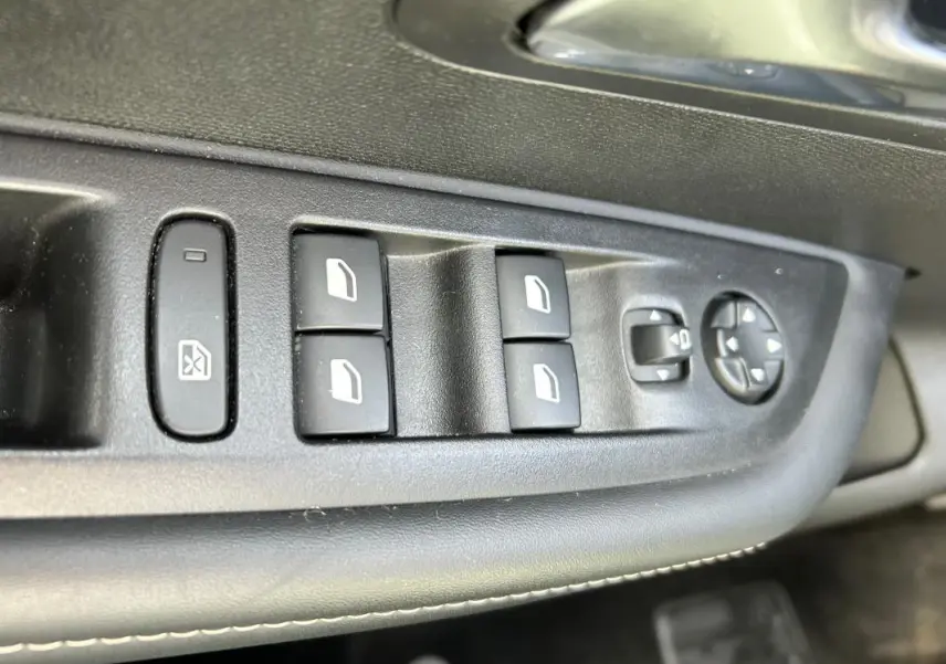 Gros plan sur les commandes des vitres électriques côté gauche d’un Peugeot 208 gris 2024 Hybrid 110 e-DCS6 Allure.
