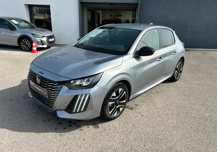 Peugeot 208 Hybrid gris vue 3/4 avant droit, avec calandre noire distinctive et jantes alliage bicolores.