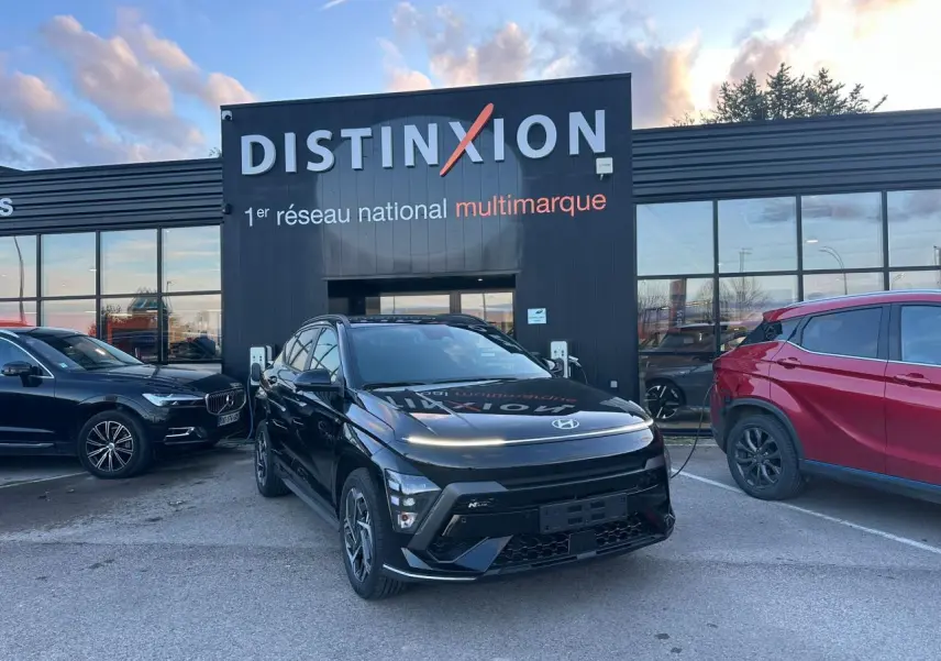 Vue 3/4 avant d'un Hyundai KONA II noir Abyss Metal avec jantes alliage et calandre marquée N Line, stationné devant un bâtiment Distinxion.
