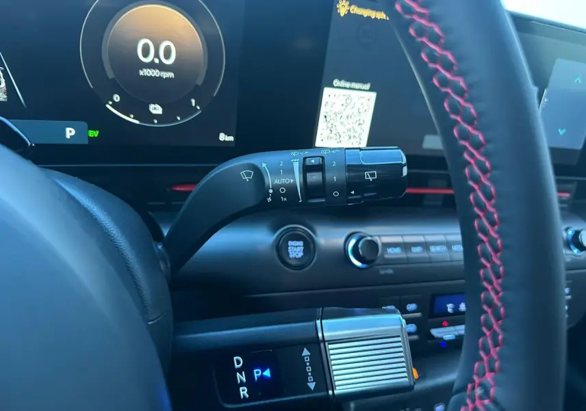 Gros plan intérieur sur la console et volant avec surpiqûres rouges du Hyundai Kona II hybride, affichage digital et commandes.