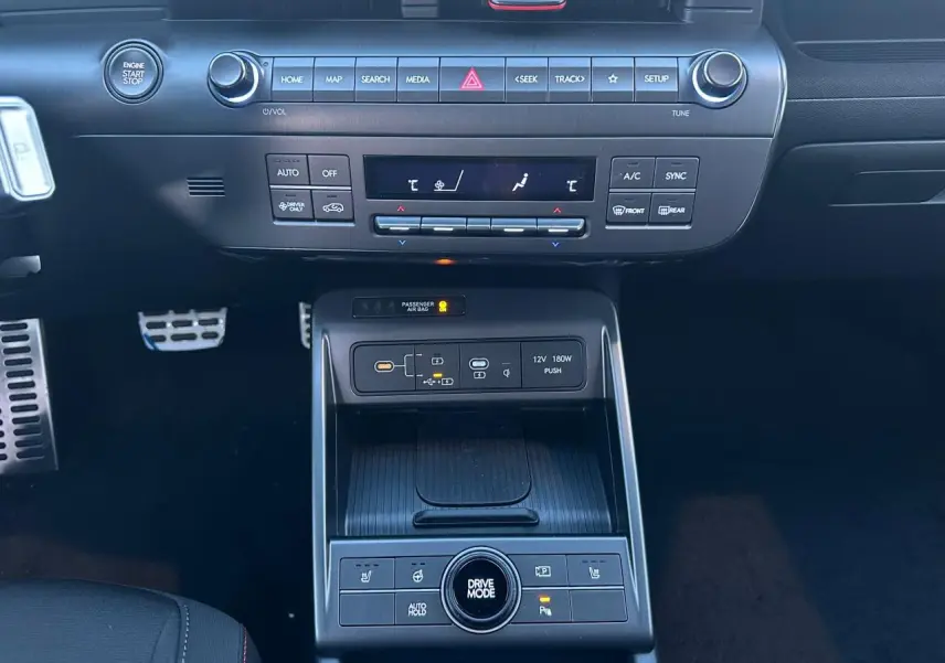 Vue centrée sur la console centrale du Hyundai KONA noir, avec commandes climatisation, chargeur sans fil et bouton Drive Mode.
