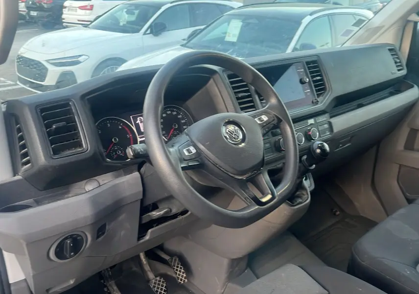 Vue intérieure côté conducteur du Volkswagen Crafter blanc, montrant le volant multifonctions et la console centrale.